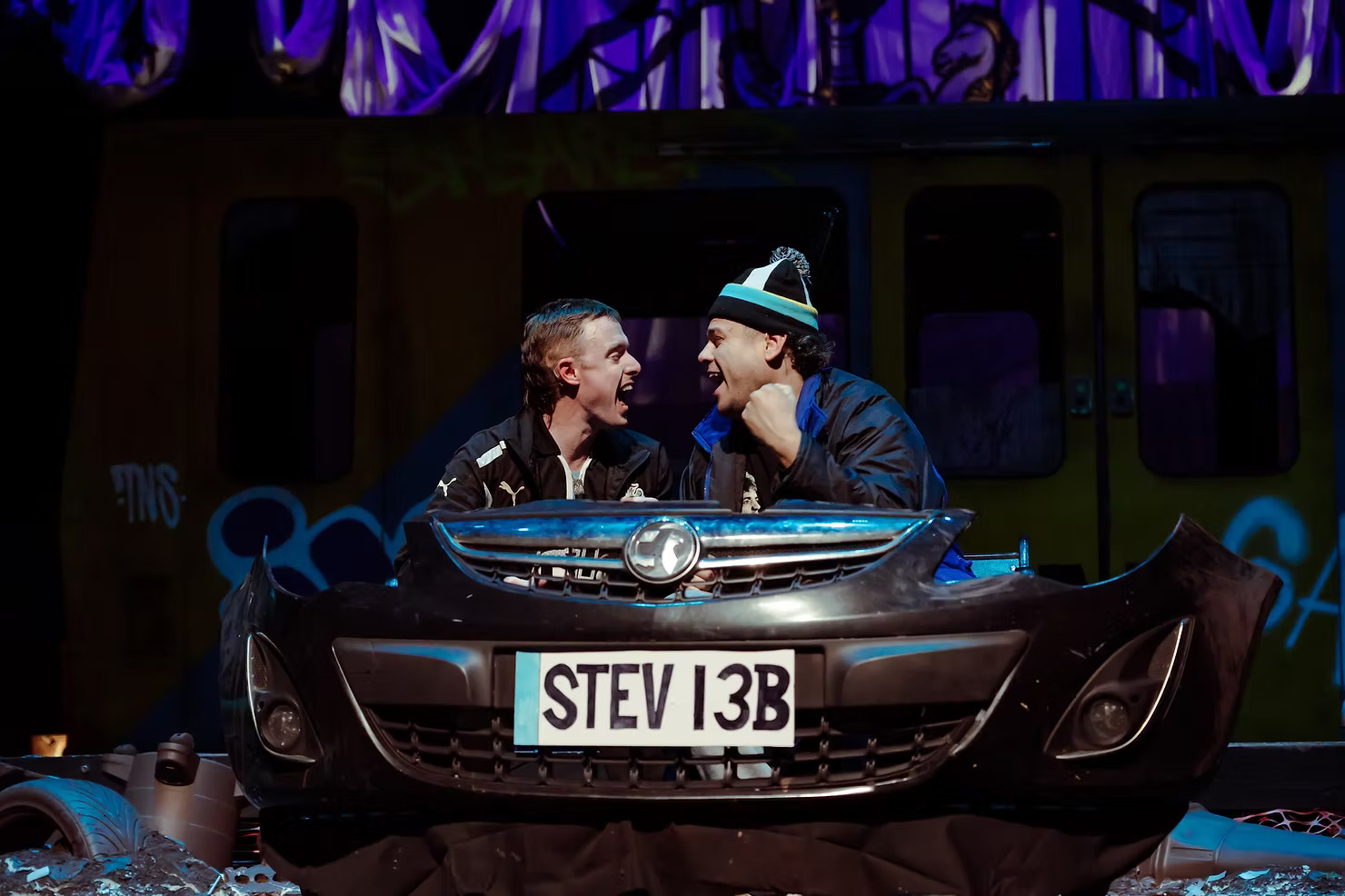Gerry and Sewell shouting to each other behind a stolen car bumper on stage